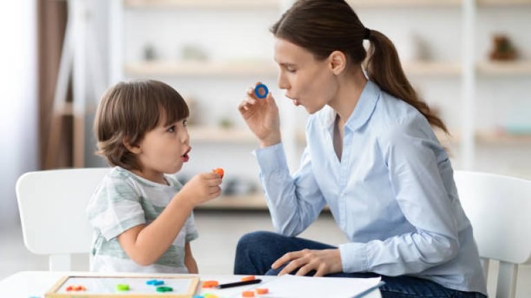 Female speech therapist curing child's problems and impediments. Little boy learning letter O with private English language tutor during lesson at office